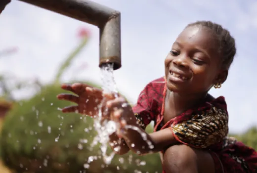 Small child smiling as they touch water coming from outdoor water faucet 